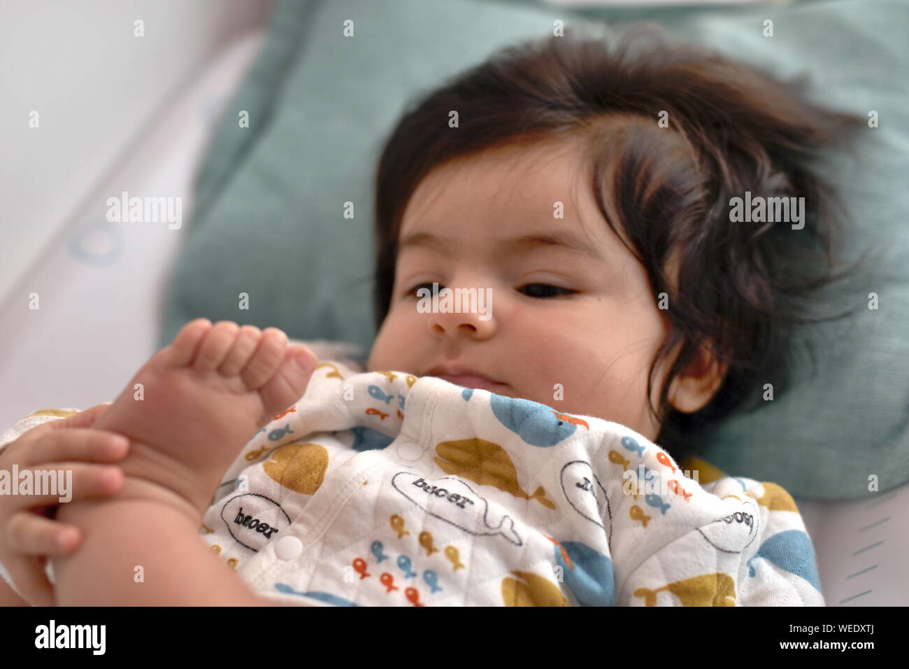 Süße langhaarige Baby prüft aufmerksam Ihre eigenen Fuß und Zehen Stockfoto