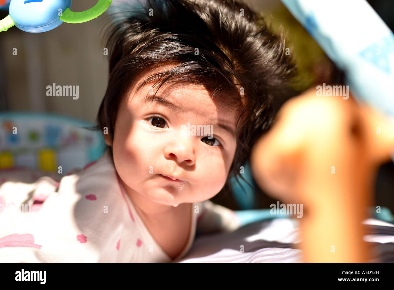 Süße Mischlinge Baby Mädchen aufmerksam in die Kamera schaut unter ihrem Spielzeug im Kindergarten Stockfoto