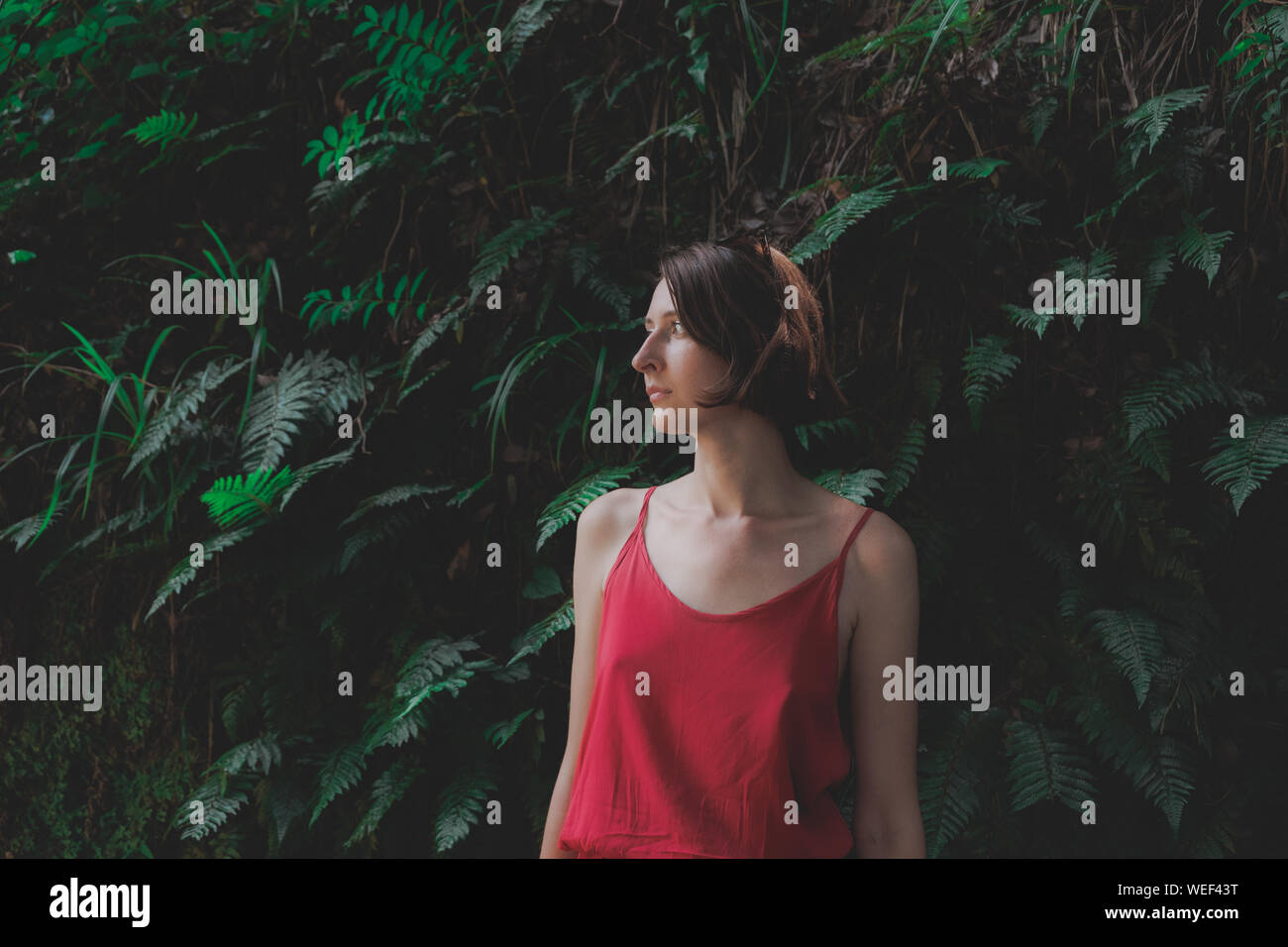 Mädchen und Pflanzen: Porträt einer schönen Frau im roten Kleid auf natürlichen, grünen Hintergrund. Schätzen, liebevolle Art Konzept: Junge weibliche steht in Stockfoto