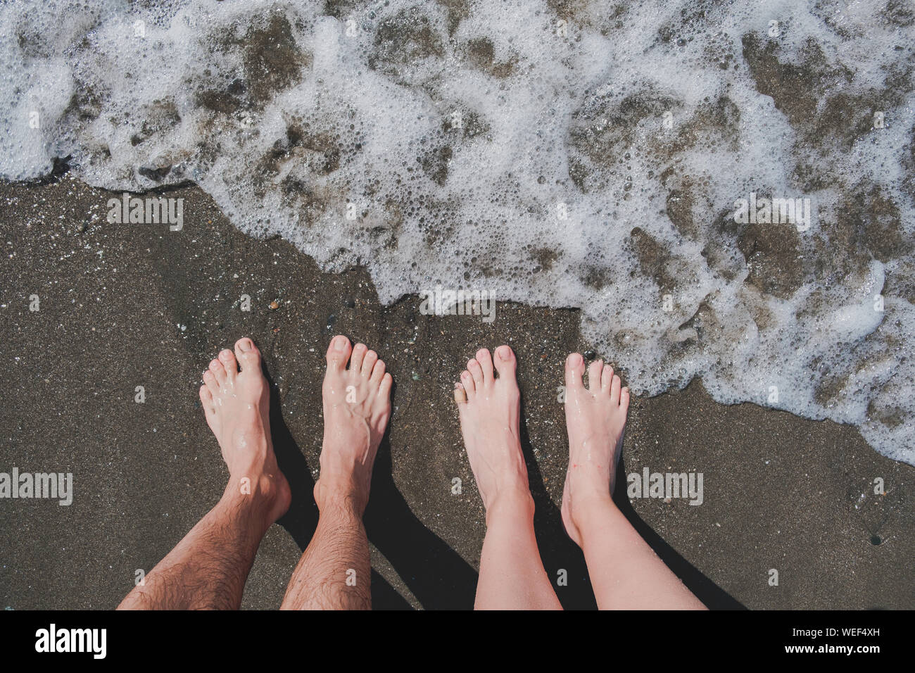 Mann und Frau stehen auf Kiesel am Meer, Sicht. Männliche und weibliche Beine am Strand, Ansicht von oben, Schwimmen im Meer und Sommerurlaub Konzept. Stockfoto
