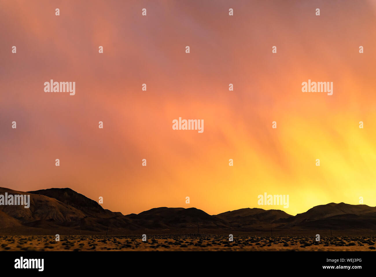 USA, Nevada, Lyon County. Einen brillanten Spritzen der leuchtend gelb, orange, rosa, lila Farben während einer westlichen Sonnenuntergang über Black Mountain Silhouetten. Stockfoto