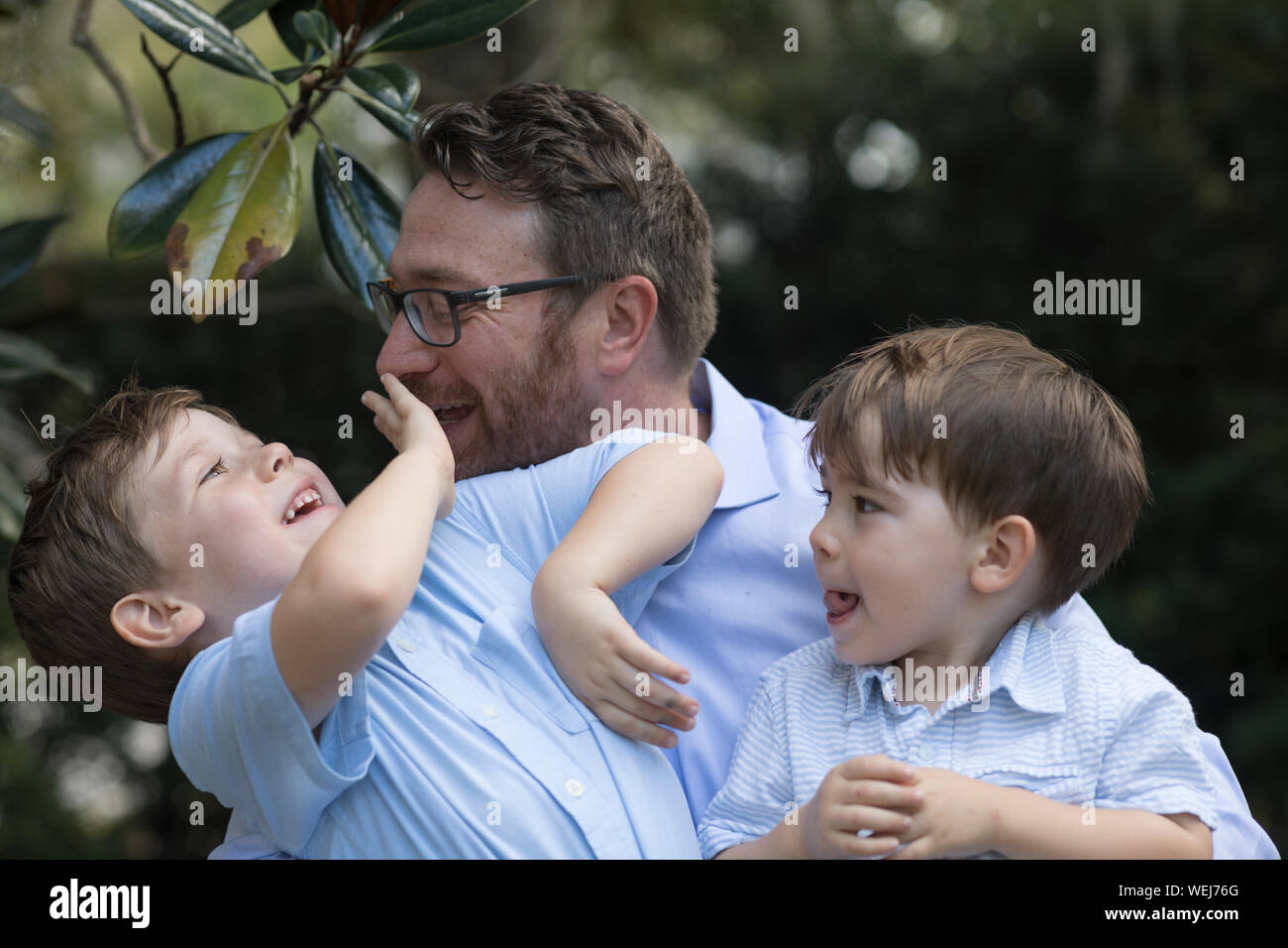 Vater mit 4 und 2 Jahre alten Söhnen sitzt auf der Bank im Park sprechen Stockfoto