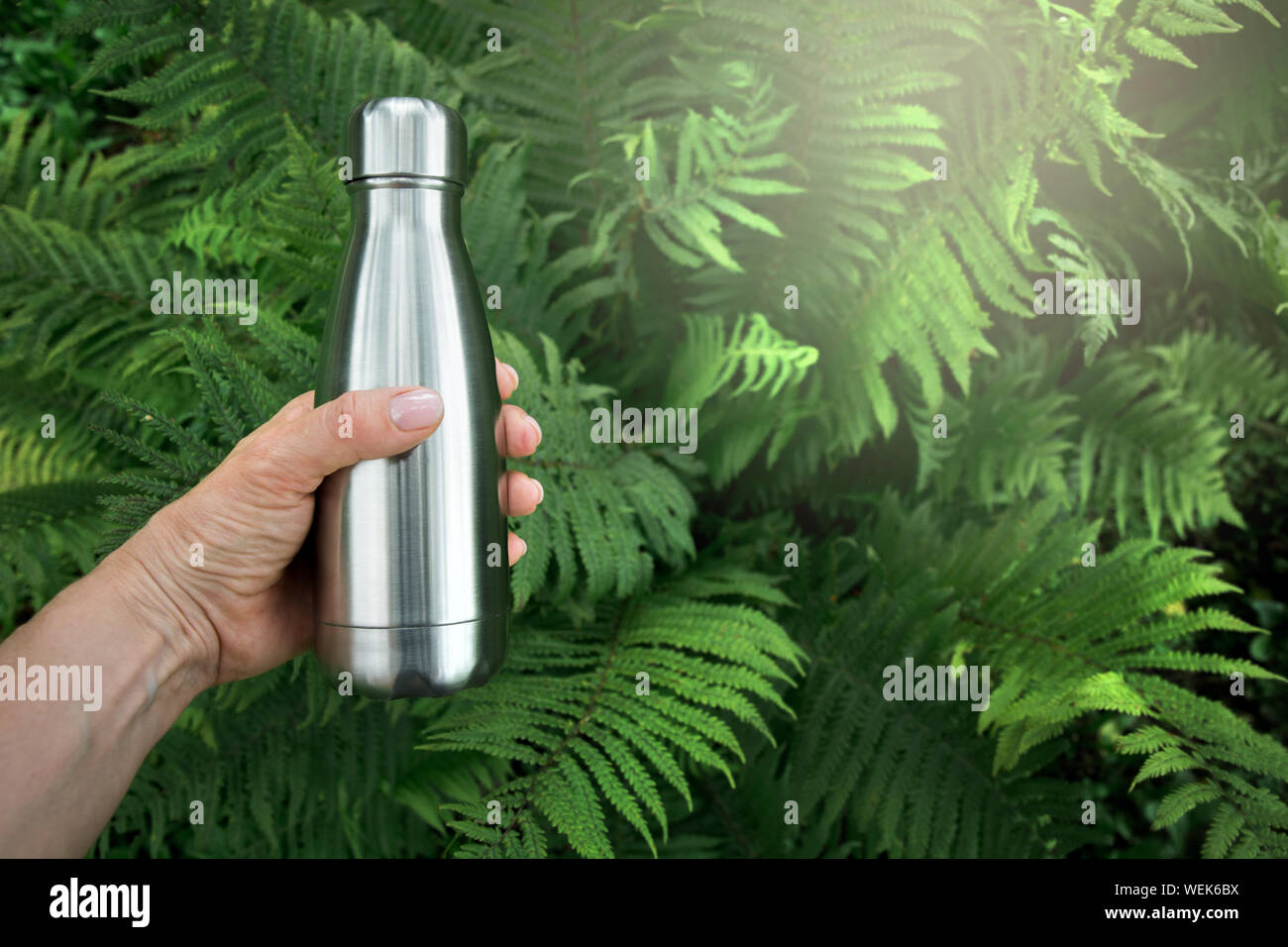 Wiederverwendbare Metall Wasser Flasche in weiblicher Hand Wasserreserven des Körpers vor dem Hintergrund der Farn Blätter in den Tropen zu ergänzen. Kein Kunststoff. Stockfoto