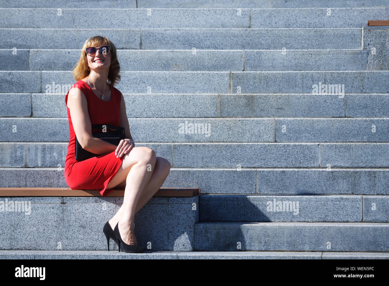 Reife Frau mittleren Alters in Rot plan sitzt auf einer Marmortreppe und lächelt, selektiver Fokus Stockfoto