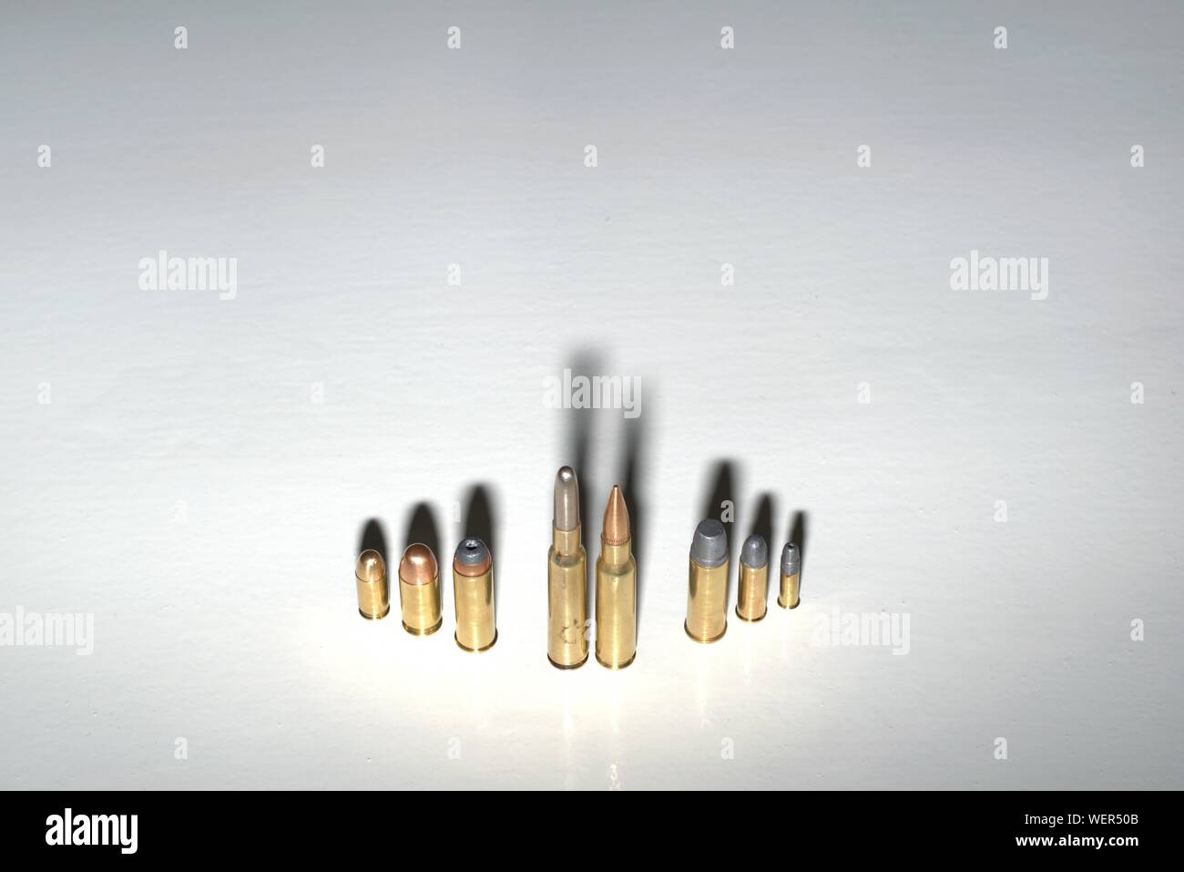 Mehrere Kugeln verschiedener Kaliber stehen auf einer weißen Fläche mit dunklen, dramatische Schatten, als Konzept zur Kriminalität Familie, Macht, Mafia, etc. Stockfoto