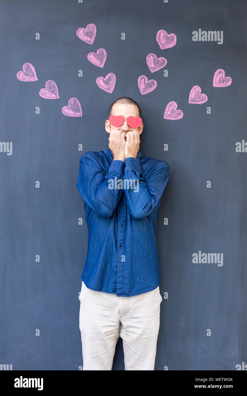 Mann mit Herz Form Papier auf die Augen gegen Tafel stehend Stockfotografie  - Alamy