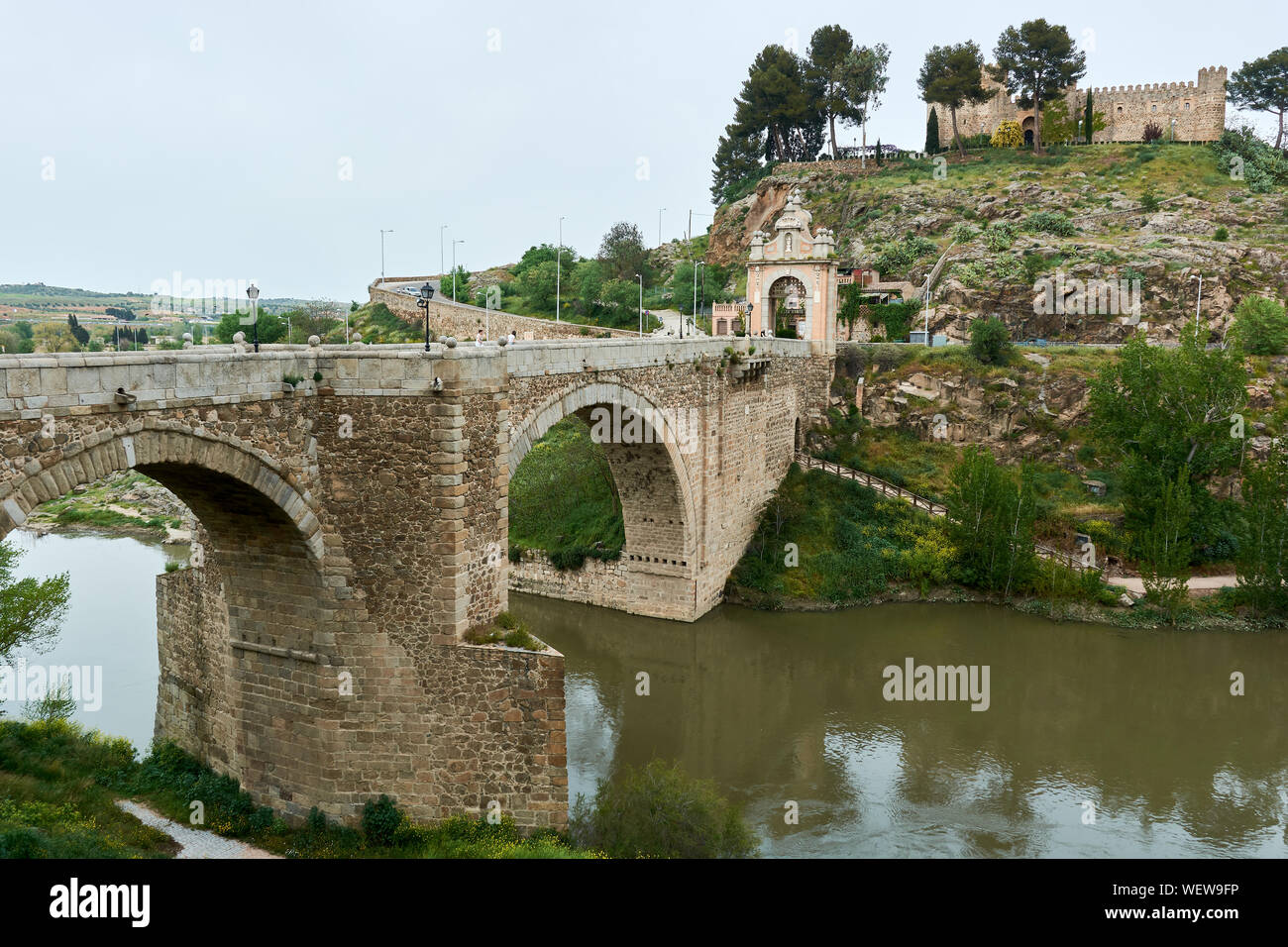 TOLEDO, Spanien - 24 April 2018: Ausblick auf die barocke Triumphbogen auf der Alcantara Brücke über den Fluss Tejo und die Burg in San Servando Toledo. Stockfoto