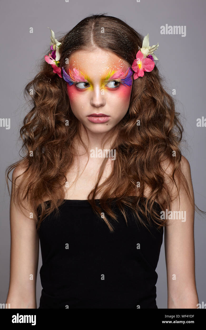 Portrait von jugendlich Mädchen mit orchideenblüte in gewelltes Haar. Junge weibliche mit ungewöhnlichen stilvolle Make-up und falsche Mode Federn Wimpern. Stockfoto