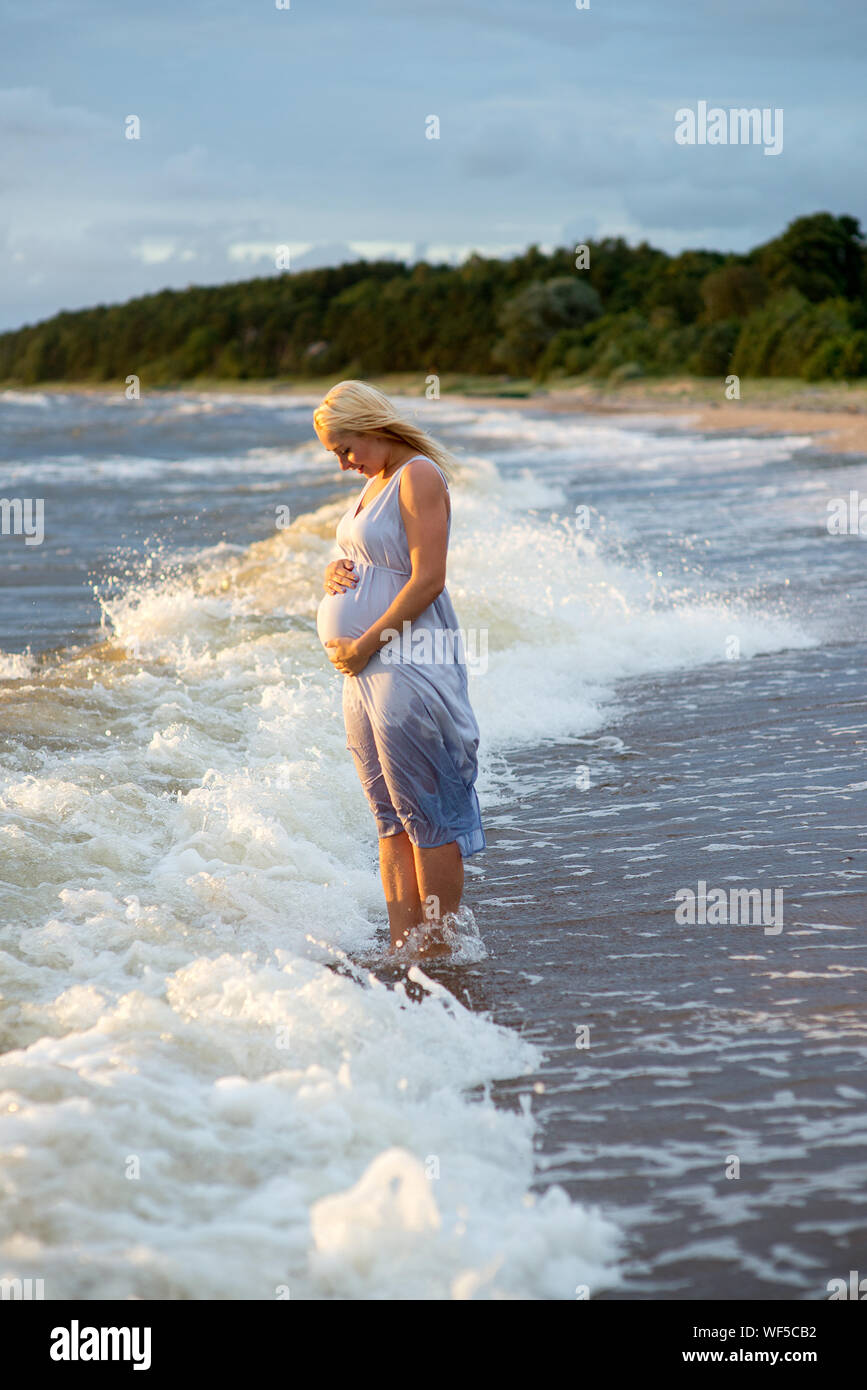 Meer Wellen Hetzen in Richtung schwangere Frau berühren Bauch Stehend am Ufer Stockfoto