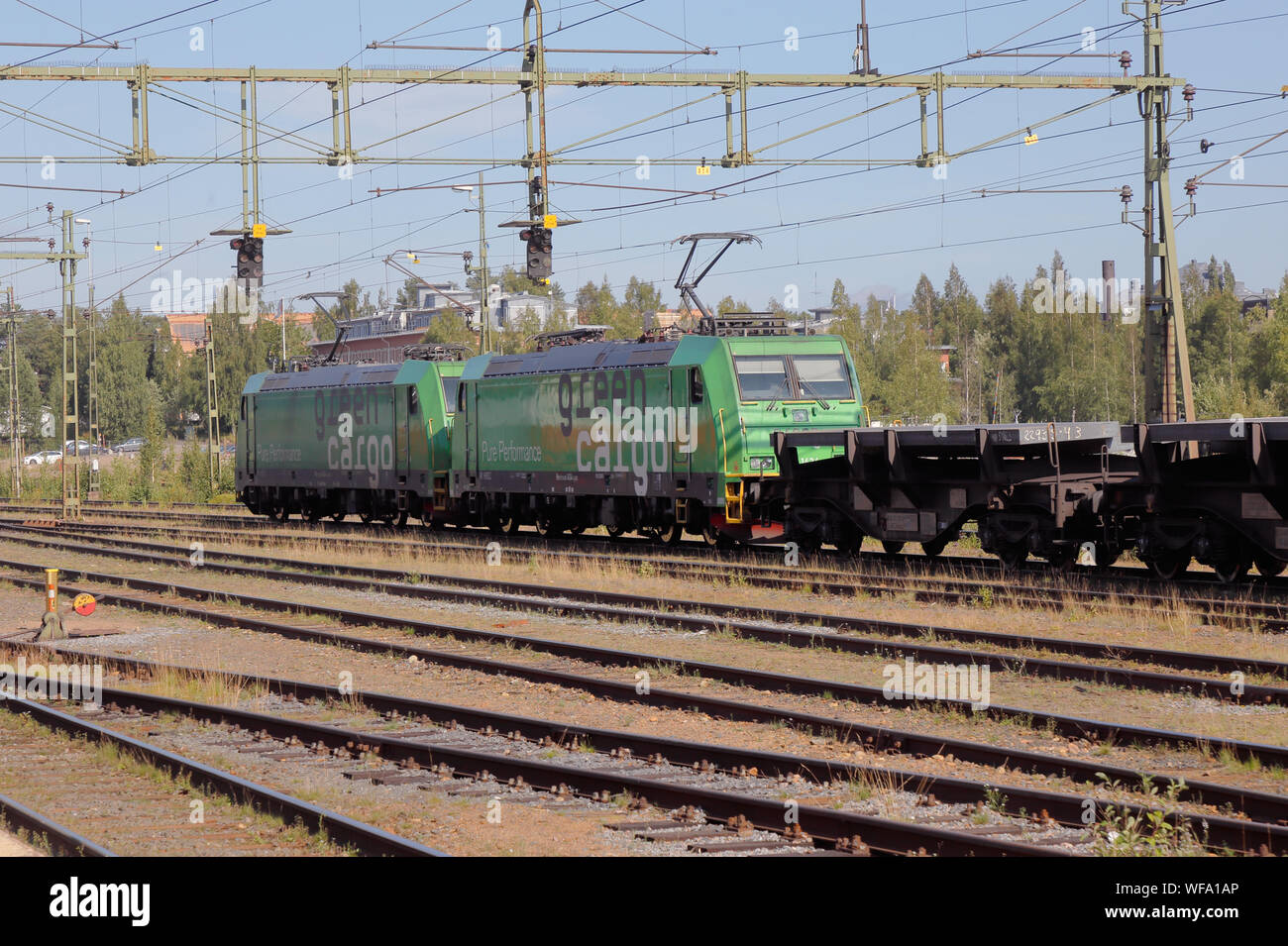 Lulea, Schweden - 20. August 2019: Zwei Green Cargo elektrische locomitives Klasse Re ziehen Flachwagen mit Stahl aus der Nähe SSAB Stahlunternehmens geladen Stockfoto