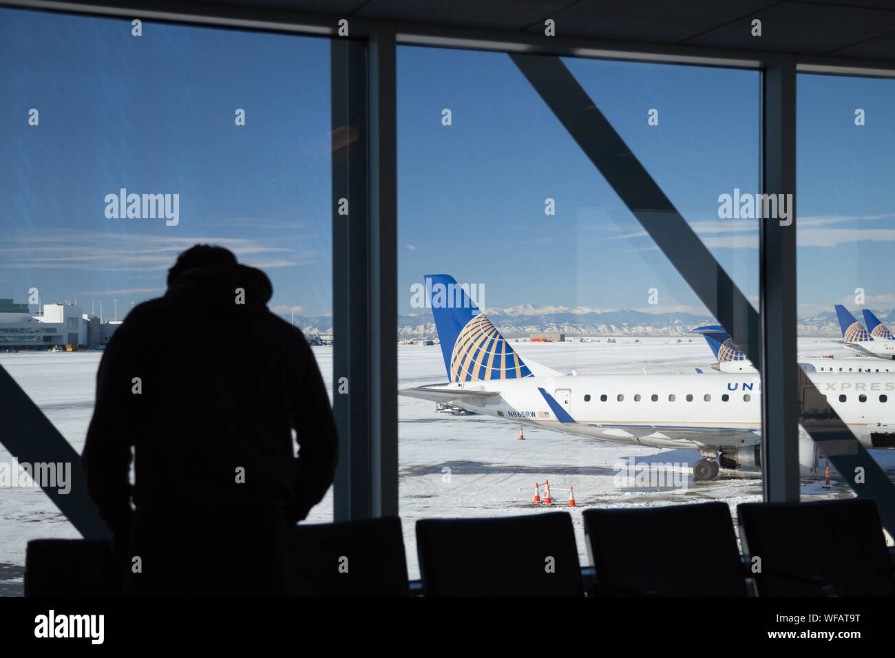 Die Silhouette eines männlichen Reisenden Blick aus Fenster wo United Airline auf dem schneebedeckten Boden am Flughafen Denver International positioniert. Stockfoto