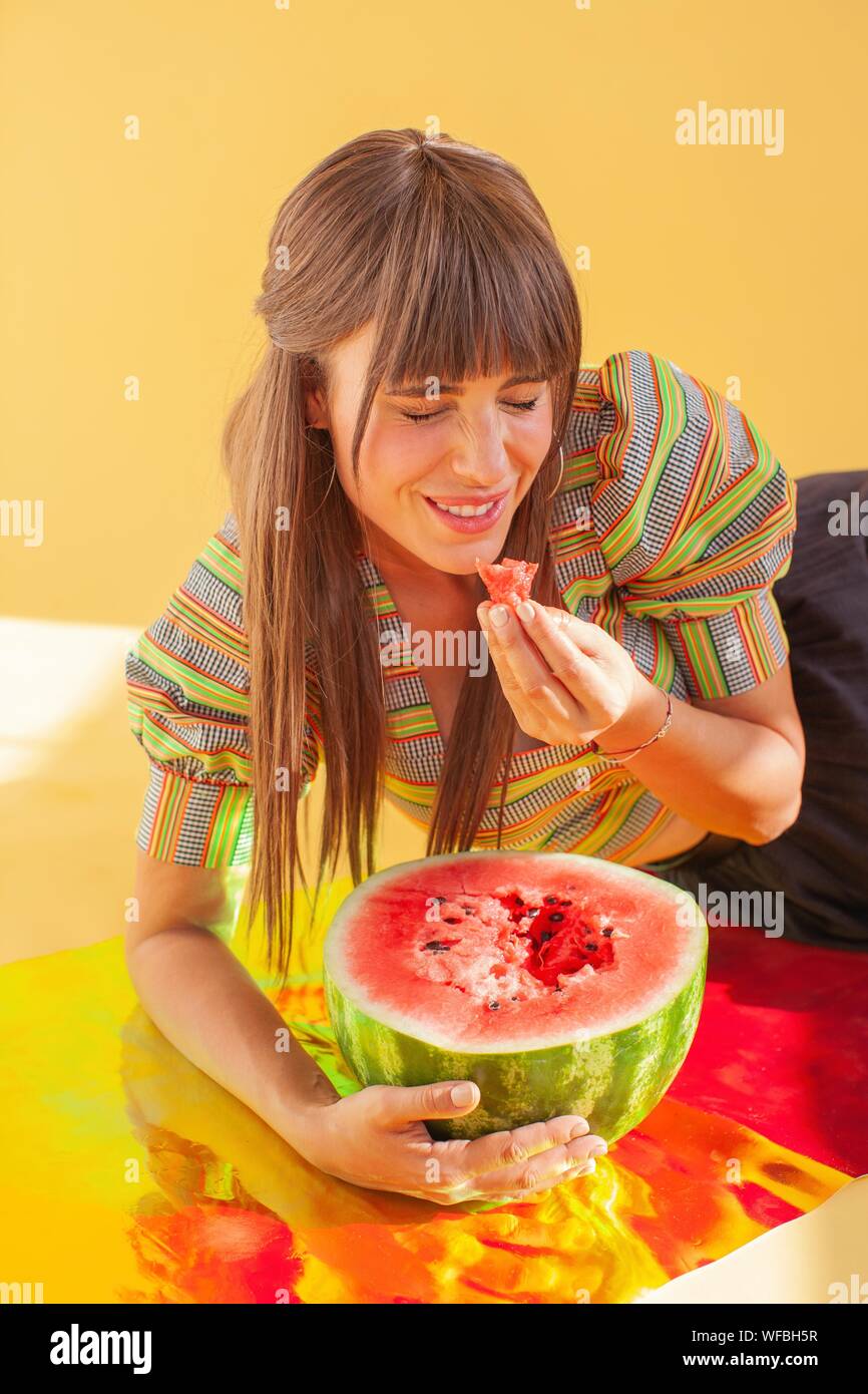 Lachende Frau sitzt auf der holografische Folie essen Wassermelone Stockfoto