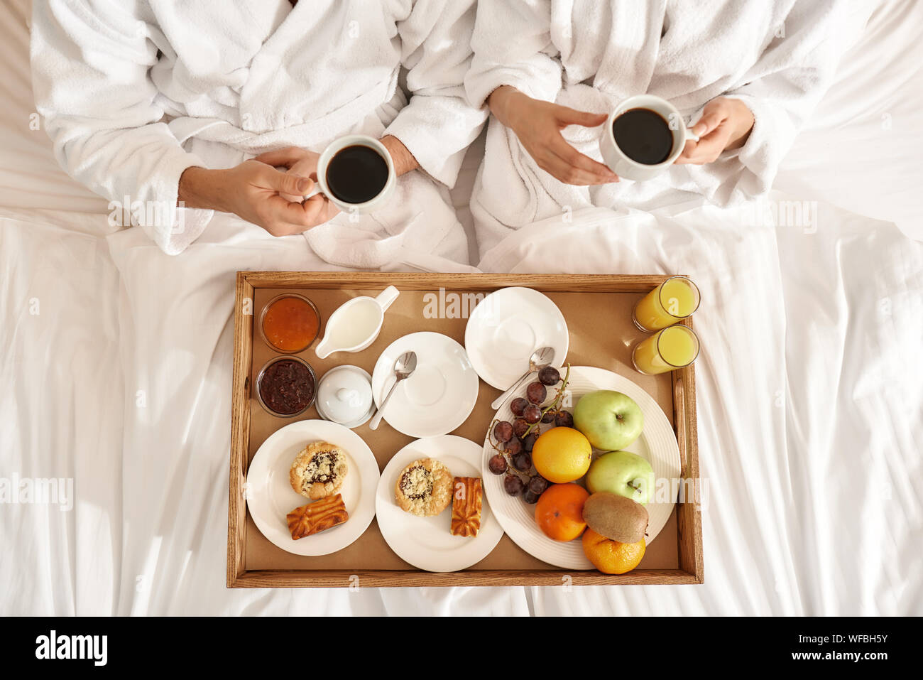 Blick von oben auf die paar tragen weiße Bademäntel im Bett lag. Das Frühstück ist auf das Fach, in das Bett. Zusammen reisen Konzept. Horizontale Schuß Stockfoto