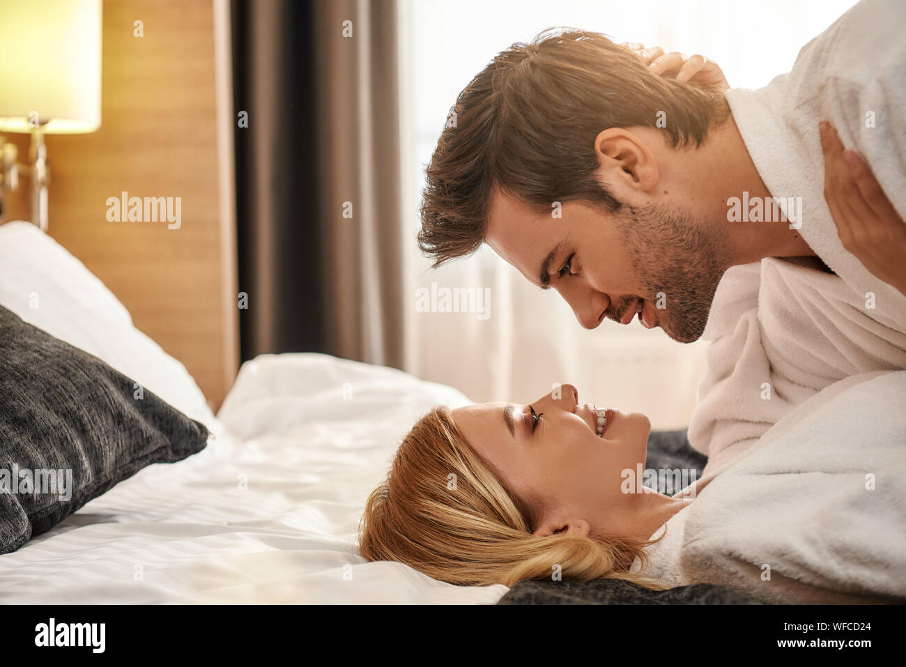 Portrait von Paar tragen weiße Bademäntel auf dem Bett liegen und sich an der Suche. Zusammen reisen Konzept. Horizontale erschossen. Seitenansicht Stockfoto