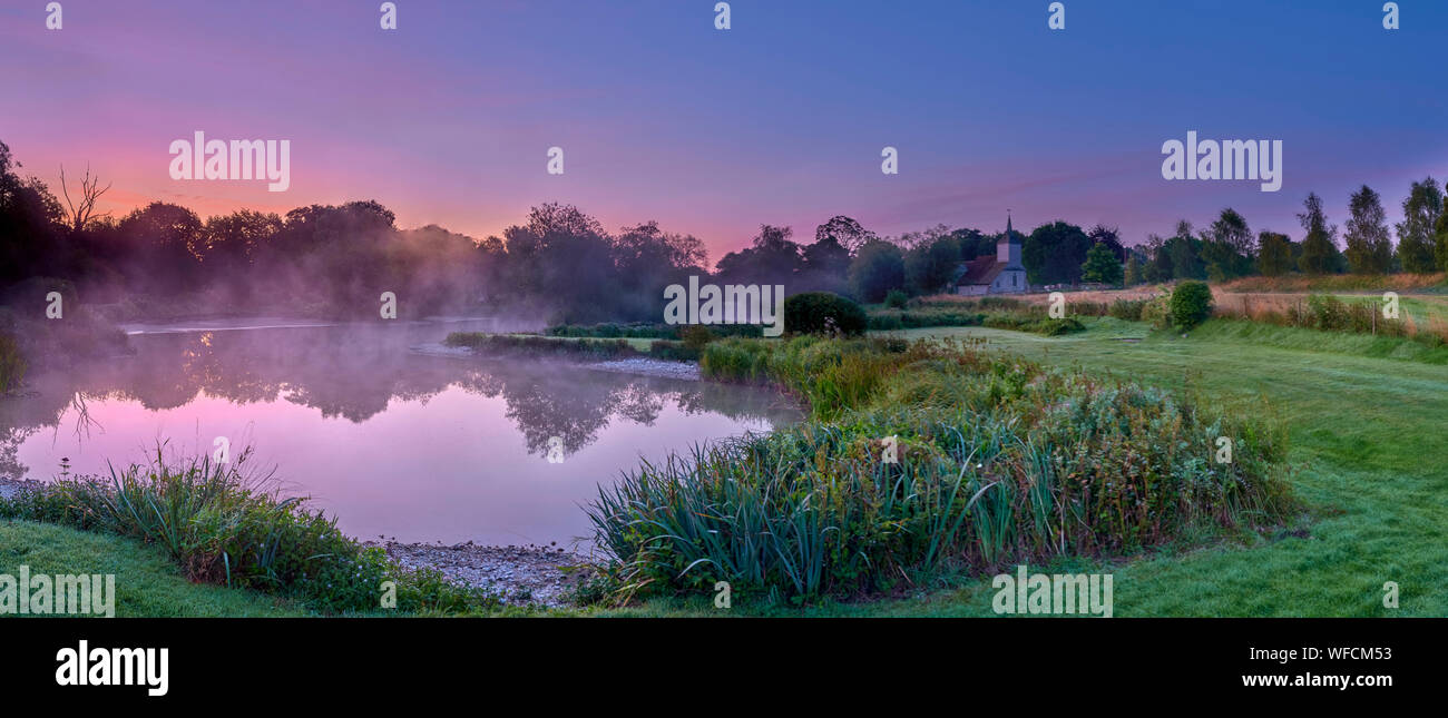 Stoke Charity, Großbritannien - 21.August 2019: Dawn Licht und Nebel auf der alten Mühle Teich im Dorf Stoke Charity mit der Kirche von St. Michael in der Dis Stockfoto