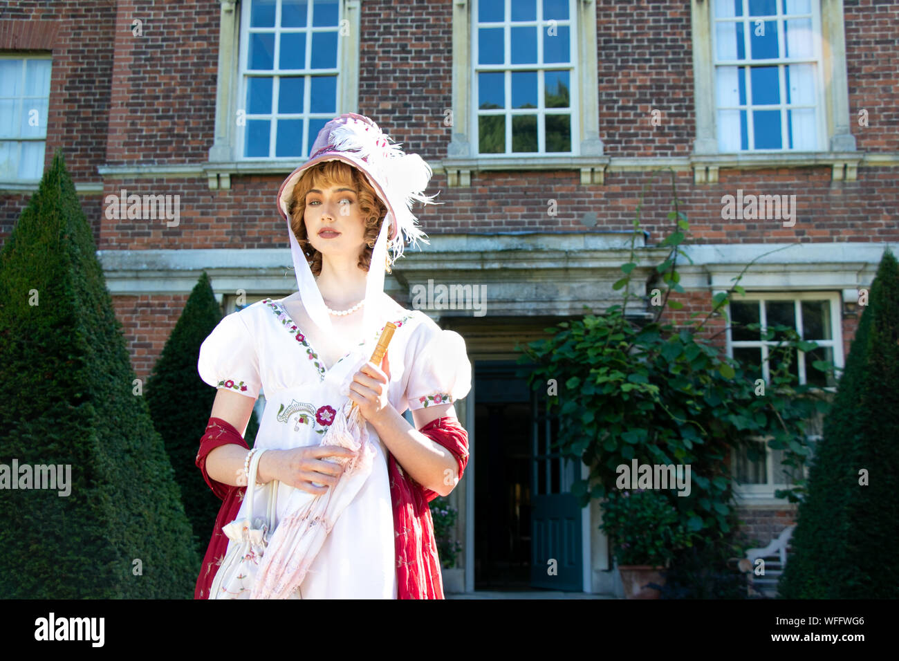 Schöne Dame tragen vintage Regency Kleid und Haube, ein Sonnenschirm und stehen außerhalb der Herrenhaus Stockfoto