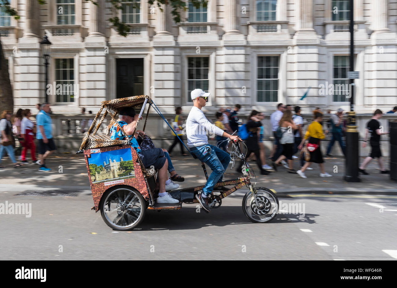 Touristen als Passagiere auf einem Sightseeing Fahrt in einem 3 Rad Rikscha oder Fahrradrikscha im Parlament Steet, Westminster, London, England, UK. Stockfoto