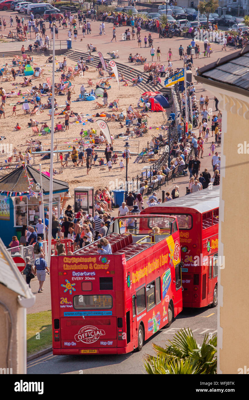 Blick von oben der Touristen, Urlauber und Besucher auf dem sandigen Strand an der viktorianischen Badeort Llandudno Wales mit oben offenen Bus Stockfoto