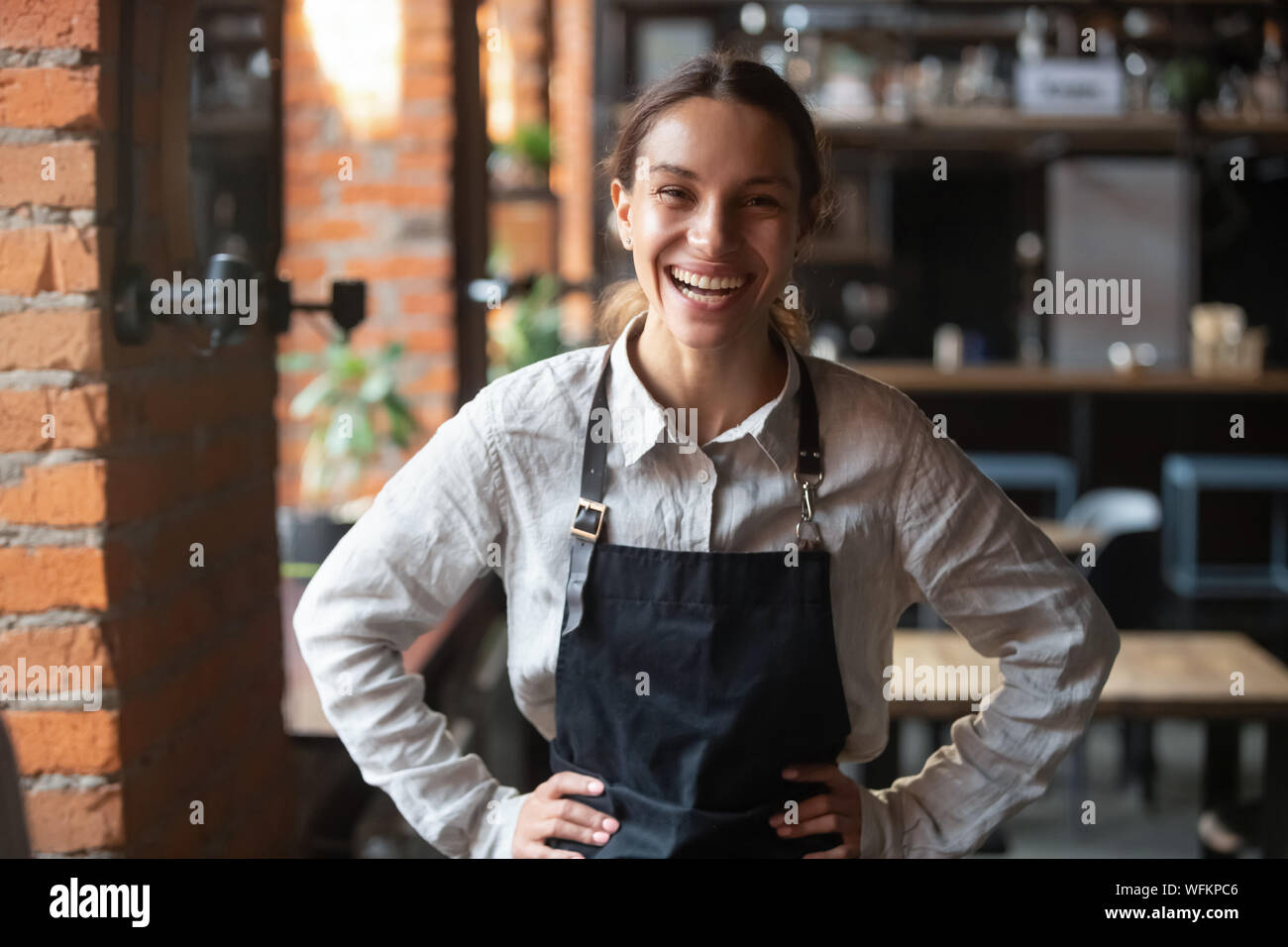 Fröhliche junge Kellnerin tragen Schürze lachend an Kamera suchen Stockfoto