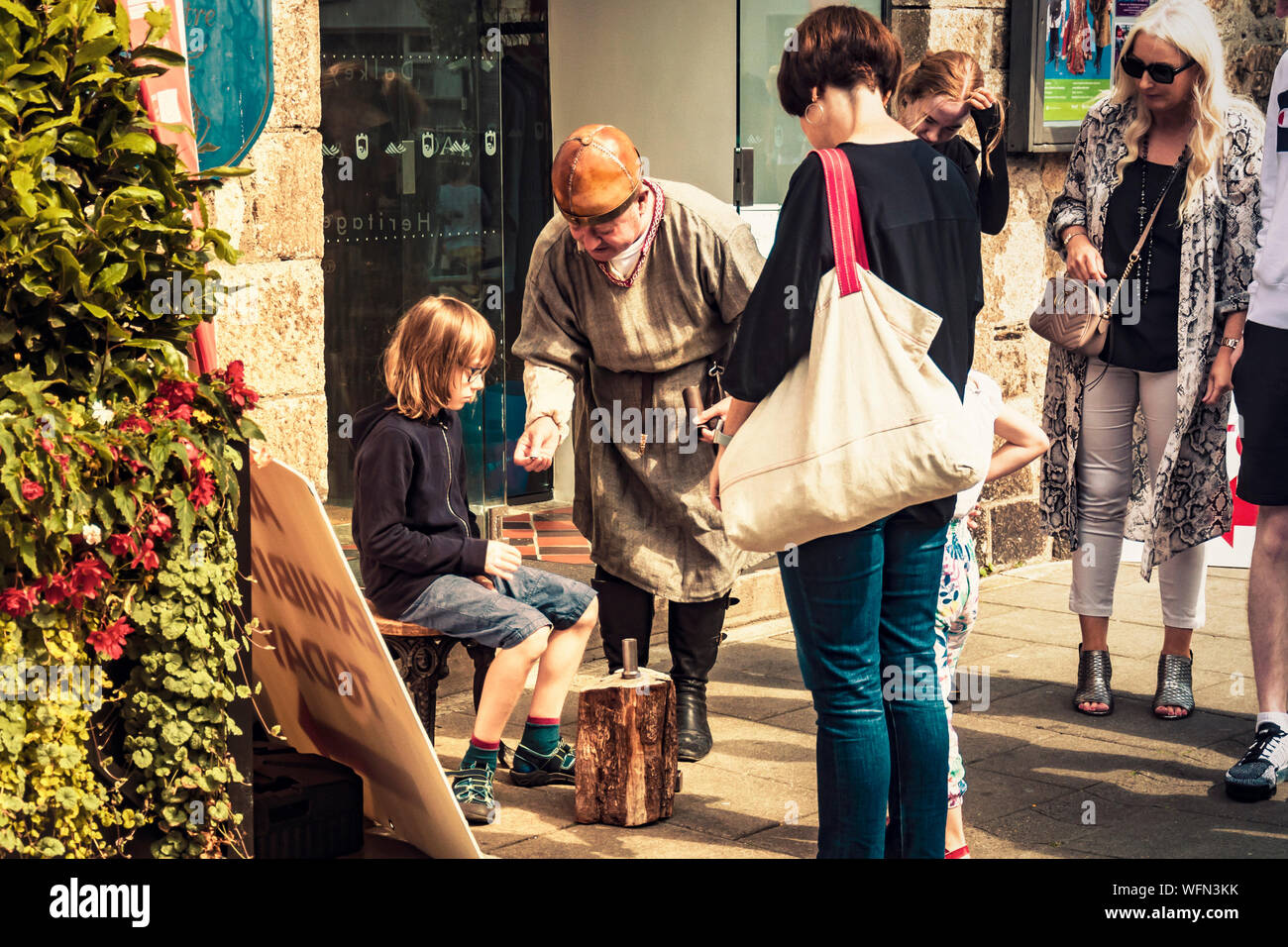 Mann in mittelalterlichen Kleidern chatten mit Jugendlichen in Gläsern und zeigte ihm, Stanz Technik alt. Dalkey, Dublin, Irland, 25. August 2019. Meeresfrüchte "Da Stockfoto