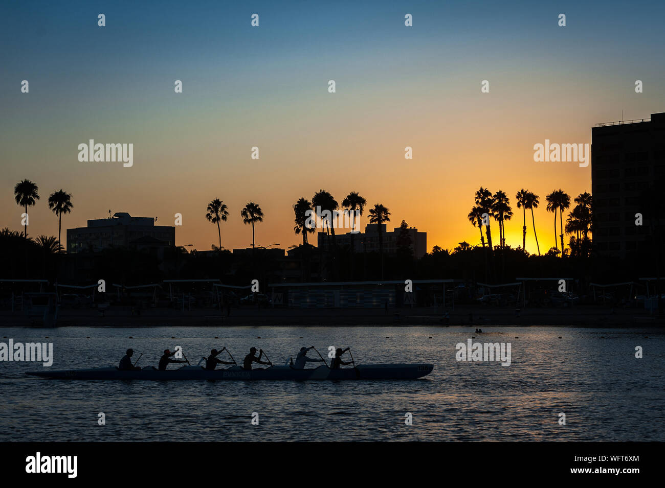 Silhouette einer Gruppe, die bei Sonnenuntergang im Hafen von Marina Del Rey in Los Angeles, CA, mit einem Auslegerkanu paddelt. Stockfoto