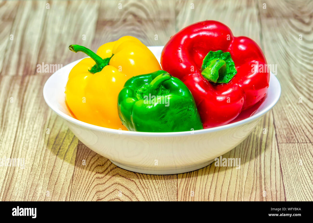 Rote, grüne und gelbe Paprika (Capsicum) in einer weißen Schüssel auf einen hölzernen Tisch. Stockfoto