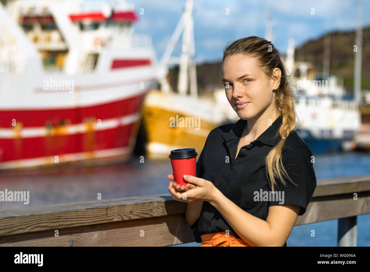 Eine junge weibliche Bedienung, die eine verfügbare Papier Tasse Kaffee suchen Kamera im Freien. Stockfoto