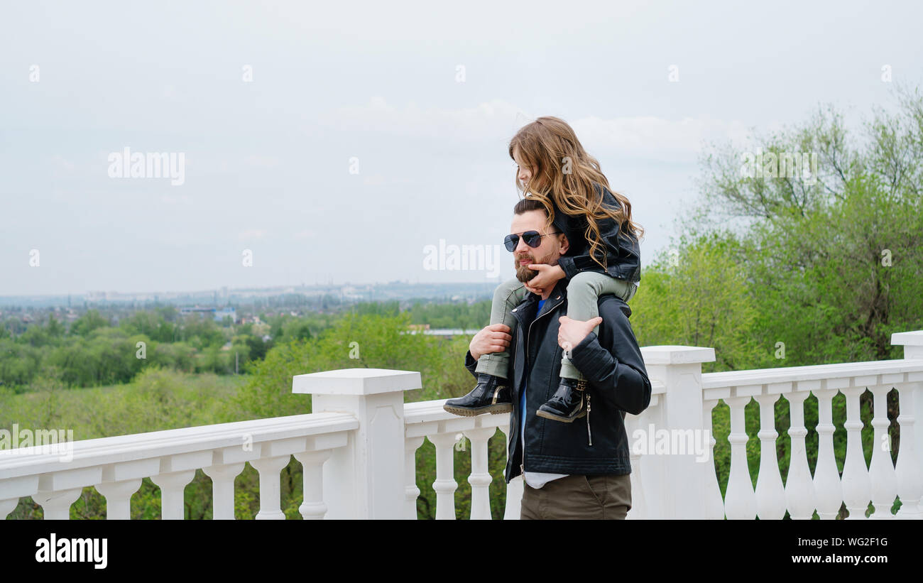 Modische stilvolle Familie für einen Spaziergang. Vati rollt seine Tochter auf seinen Schultern. Spaziergang auf der Aussichtsplattform. Zeit zusammen. Familie suchen. Urban casual Stockfoto