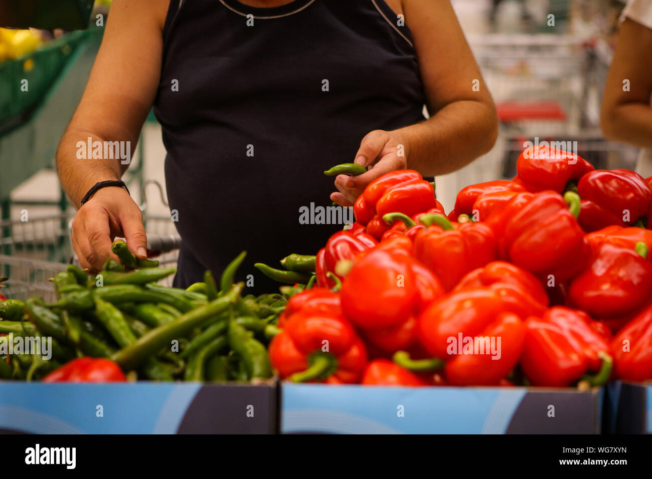 Details of a man choosing hot green peppers (sweet red peppers also on the shelf) on the fruits and vegetables aisle in a store Stockfoto