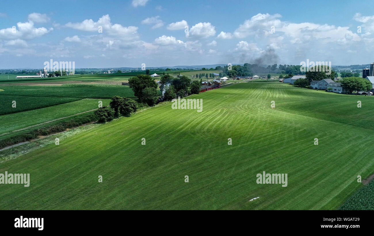 Eine Luftaufnahme von einer Dampflok der Ankunft in Amish Landschaft an einem Sommertag, wie gesehen, die von einer Drohne Stockfoto
