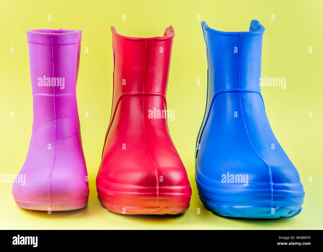 Rot Blau und Rosa Gummistiefel EVA auf gelbem Hintergrund. Stockfoto