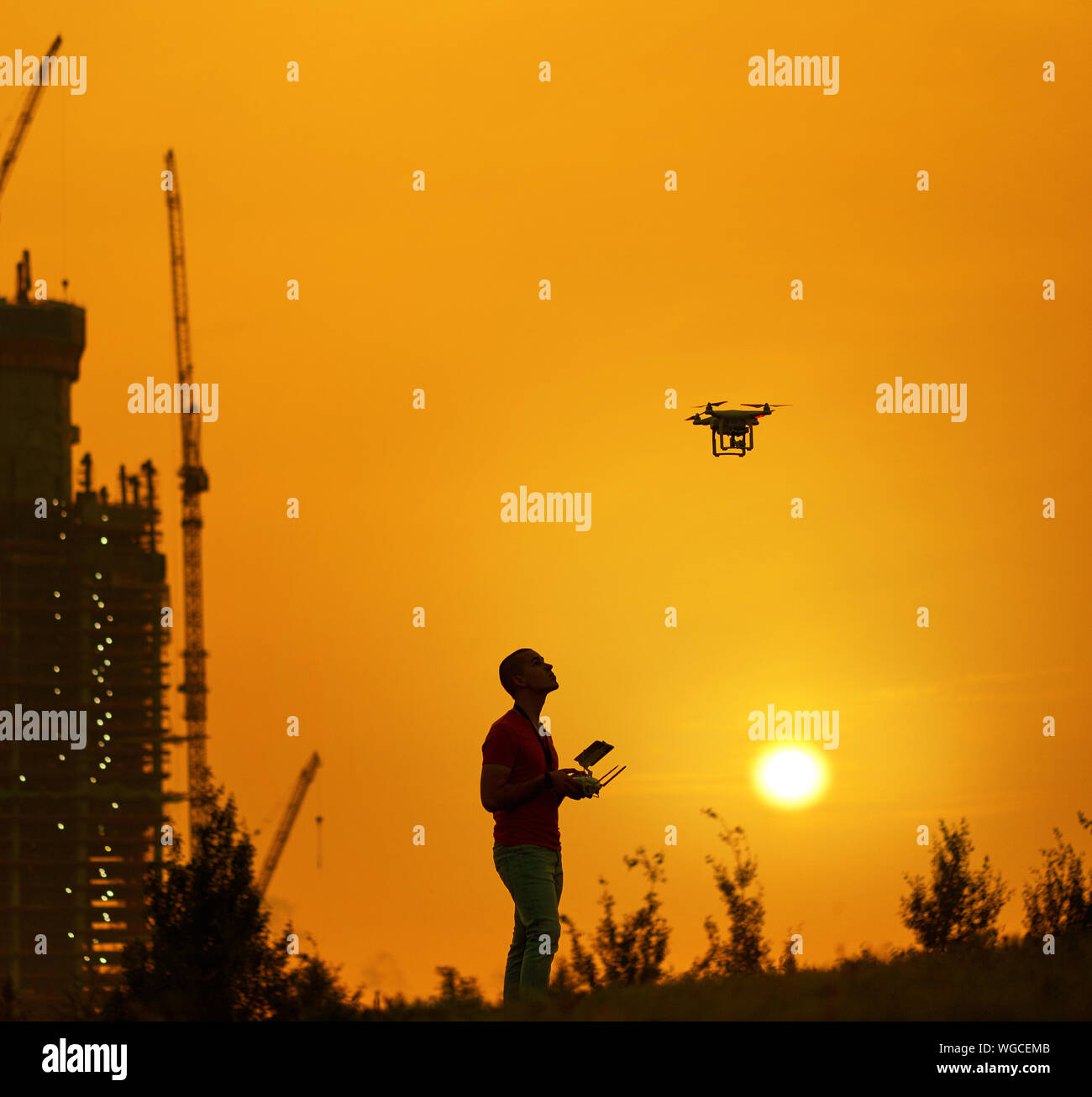 Man steuert einen quadrocopter am warmen Sonnenuntergang. Neues Gebäude für den Hintergrund. Stockfoto