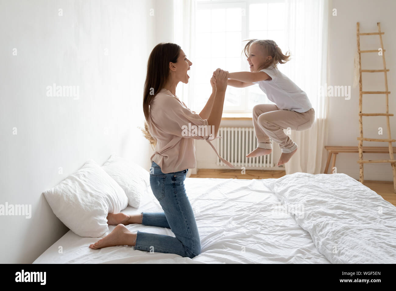 Kleine Tochter frolics Springen auf Bed Holding Mütter Hände Stockfoto