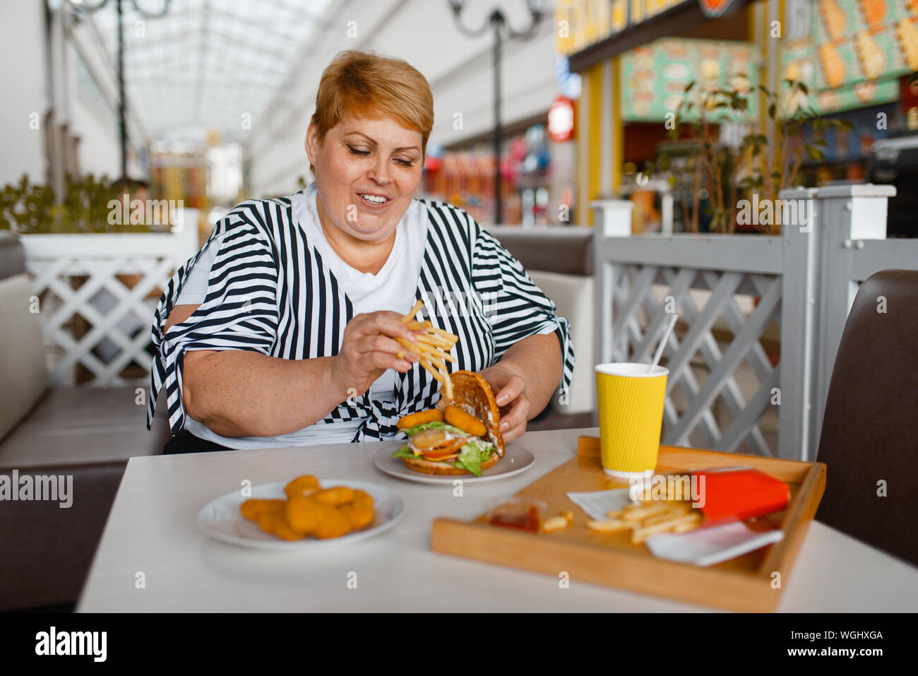 Fette Frau essen kalorienreiche Lebensmittel in der Mall Stockfoto