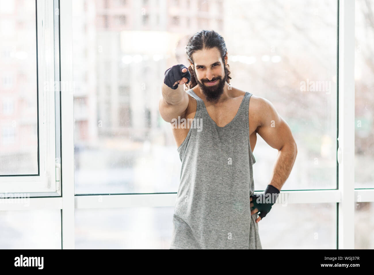 Mögen Sie Sport? Junge muskulöse Trainer Mann mit lockigem Haar lang ständigen Zufrieden, auf Sie zeigenden Finger, Fragen über Sport, Hand auf Stockfoto