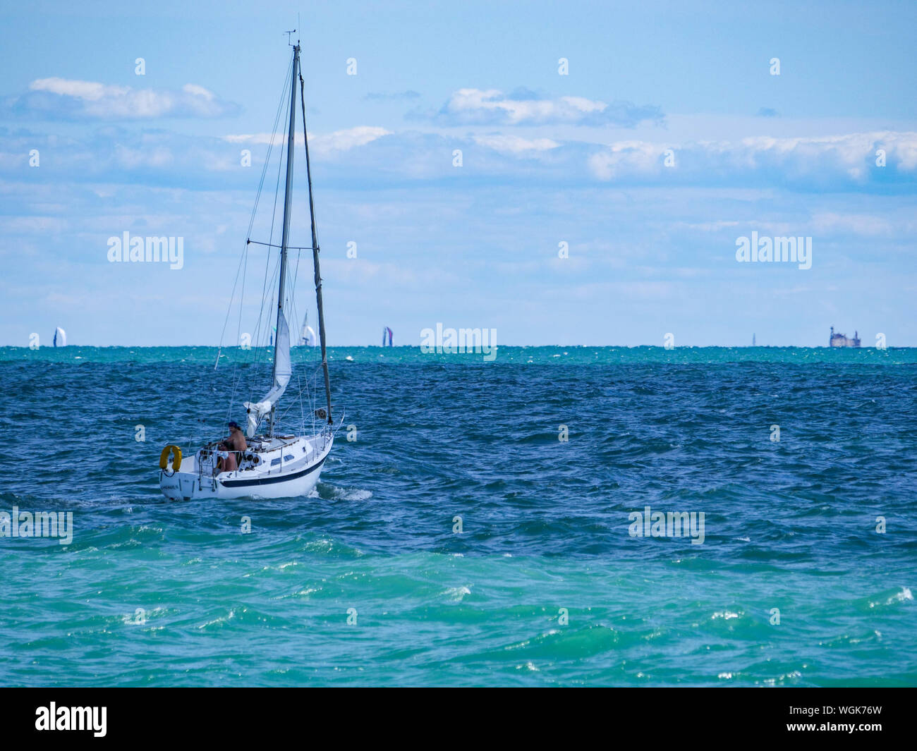 Ein Segelboot navigieren im kabbeligen Wasser des Lake Michigan aus Chicago. Die Masten von weit entfernten Segelboote Peek über dem Horizont in der Ferne. Stockfoto