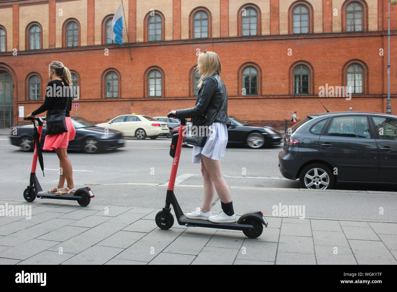 E Mobility, zwei junge Frauen auf E Scooter, München Ludwigstraße vor dem Universitätsgebäude. Stockfoto