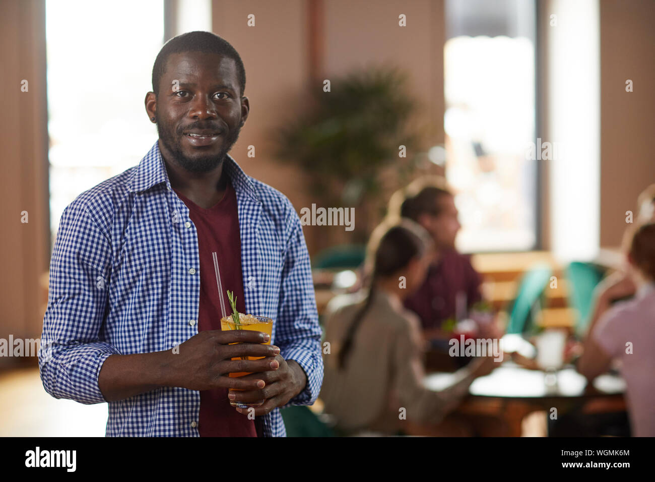 In warmen Farbtönen Taille bis Portrait von afroamerikanischen Mann lächelnd in die Kamera halten und Getränk im Cafe, kopieren Raum Stockfoto
