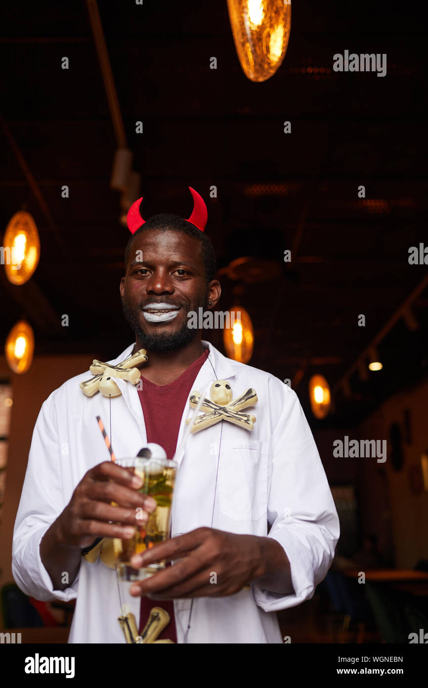 Taille bis Portrait von afro-amerikanischen Mann, der Halloween Kostüm posiert mit Getränk während der Party im Night Club, kopieren Raum Stockfoto