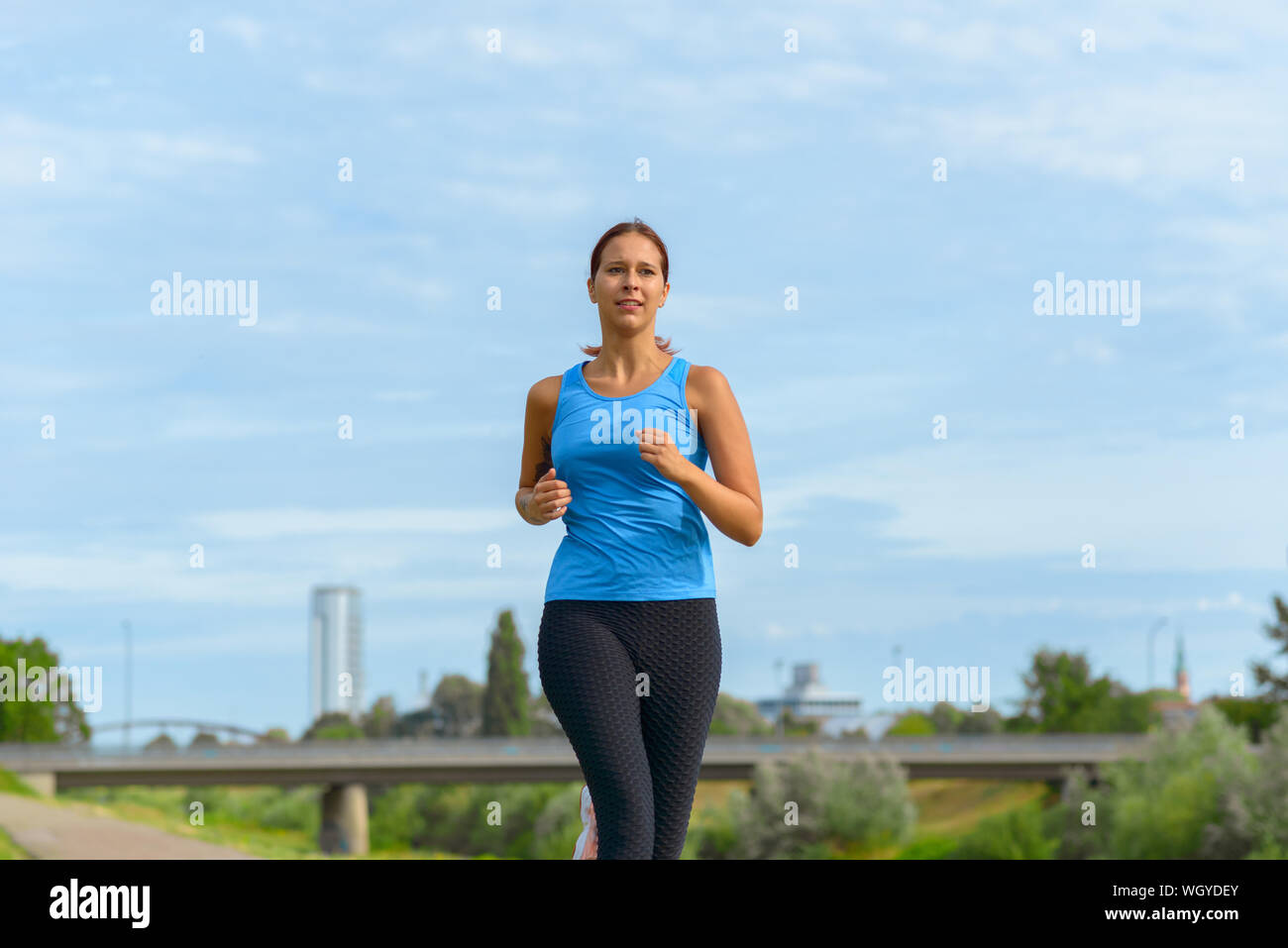 Frau Joggen im Freien im Sommer Sonne nähert sich die Kamera in einem niedrigen Winkel drei Viertel Ansicht konzeptionelle Gesundheit und Fitness Stockfoto