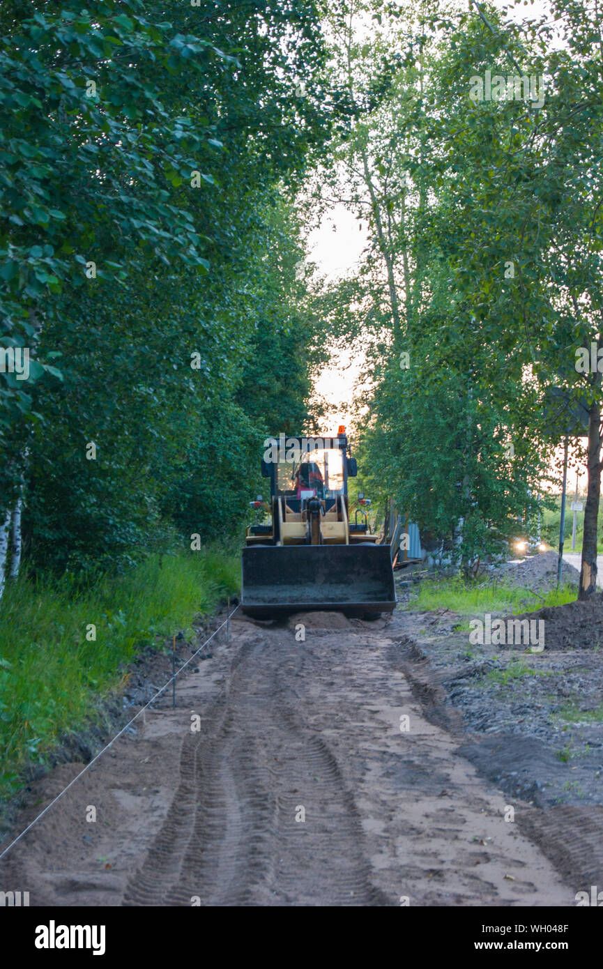 Straße Reparaturarbeiten - eine gelbe Schlepper steht auf dem Bürgersteig, die Reparatur wird. Im Vordergrund ist ein Sandweg. Vertikale Foto Stockfoto