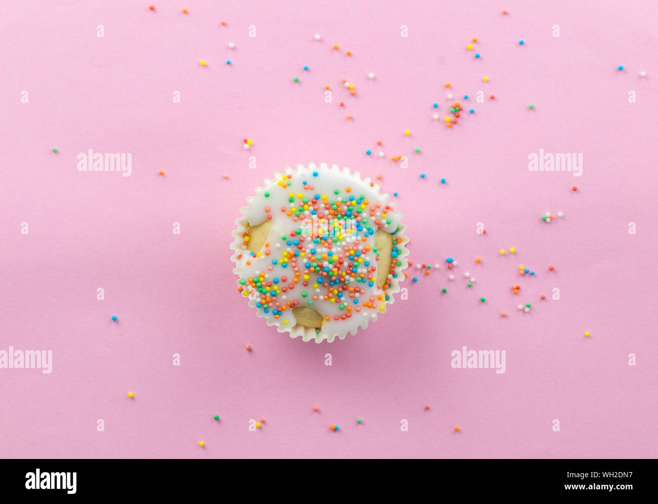 Kleine Milchglas Cupcake im Zentrum von rosa Hintergrund mit bunten Streuseln Runde auf Rosa mit Kopie Raum - oben viiew Foto sprengte Stockfoto