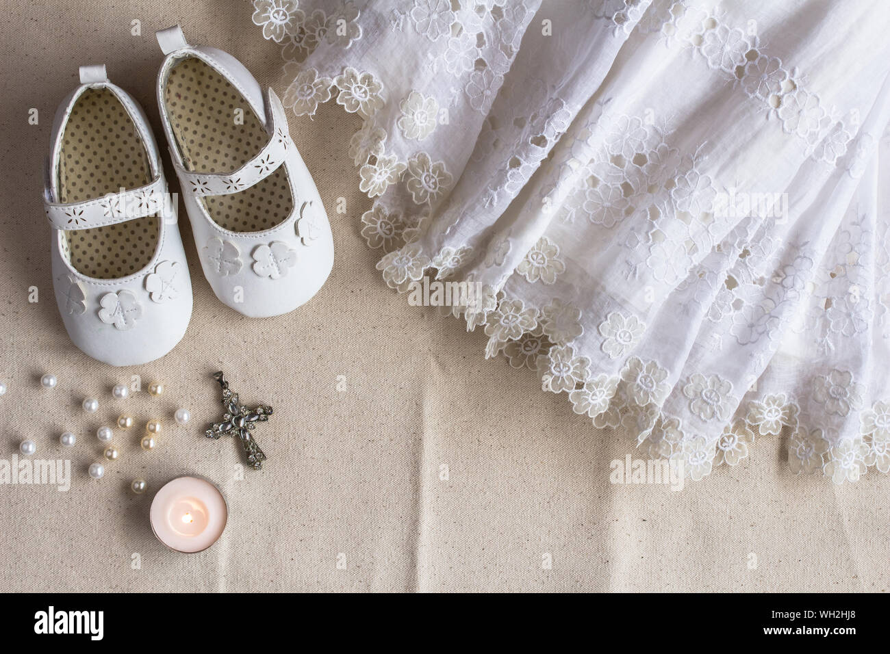 Taufe Hintergrund mit Taufe Kleid, Schuhe, Kerzen und Kristall Kreuz Anhänger auf weißem Leinen Stockfoto