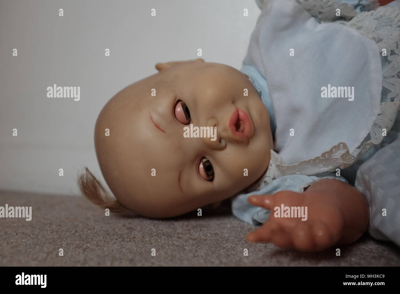 Alt, abgenutzt und schmutzig Spielzeug Puppe mit einer unheimlichen, in der Ecke eines Zimmers liegen. Stockfoto