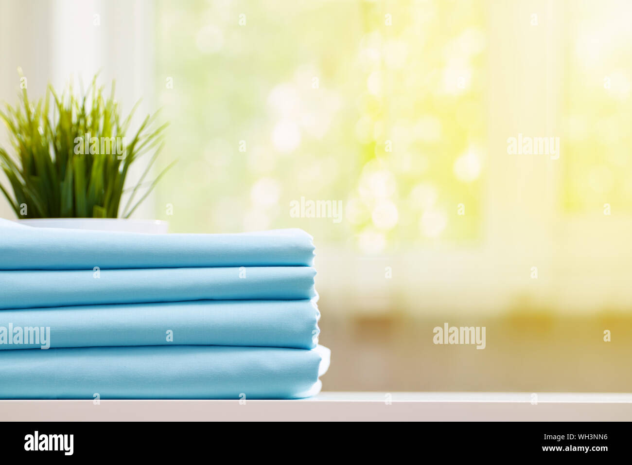 Nahaufnahme des Blauen saubere Betten auf einer verschwommenen Hintergrund. Ein Stapel gefalteter neue Bettwäsche auf dem Tisch. Sonnenlicht aus dem Fenster. Stockfoto