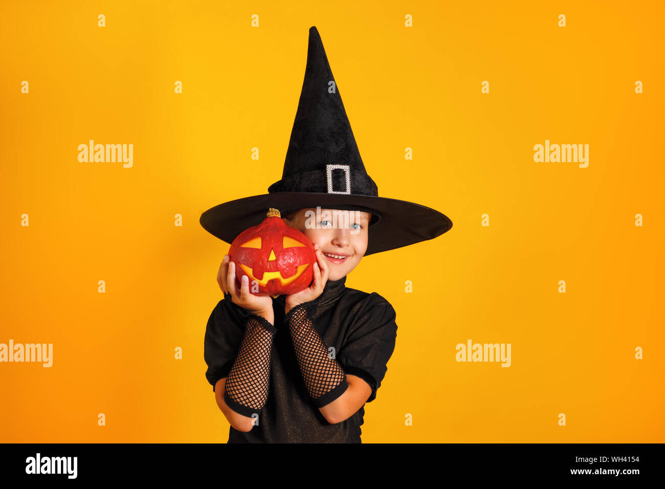 Süße kleine Mädchen in eine Hexe Kostüm hält einen Kürbis jack Lantern auf gelbem Hintergrund. Halloween Feier. Stockfoto