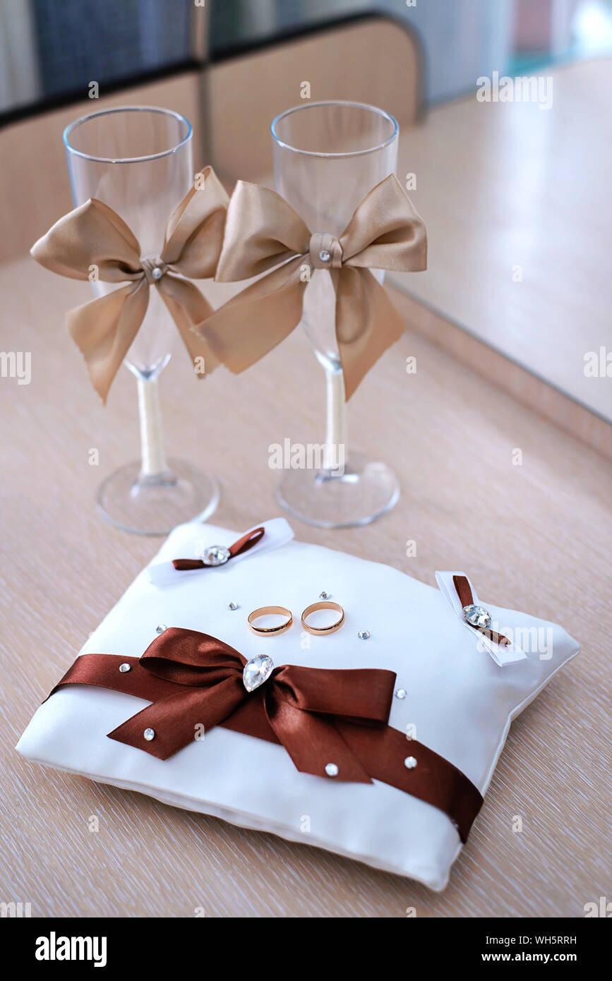 Gold Trauringe auf weißem Kissen mit Brown Bug und Gläser Stockfoto