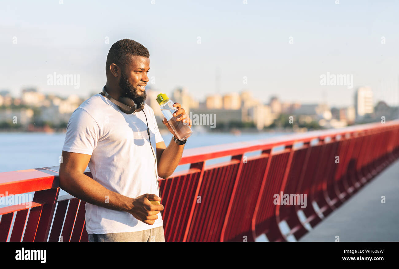 Junge schwarze Kerl Trinkwasser, bleiben auf der Brücke Stockfoto