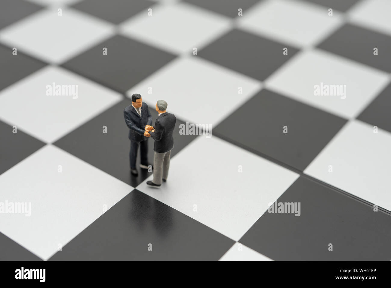 Miniatur 2 Personen Unternehmer Hände schütteln, stehend auf einem Schachbrett mit einer Schachfigur auf der Rückseite der Aushandlung im Geschäft. Als Hintergrund Business Con Stockfoto