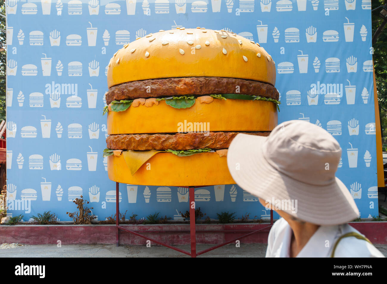Eine einheimische Person mit Hut sieht sich die riesige Burger-Requisite als Werbung für die Eröffnung von MacDonald in naher Zukunft an. Ho-Chi-Minh-Stadt, Vietnam. Stockfoto